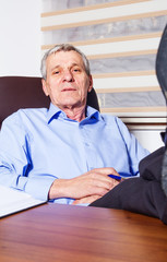 Senior businessman lying on his office chair with his feet on th
