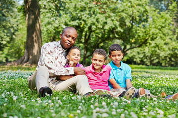 Father and three sons sit on ground in summer park