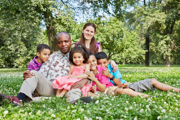 Fototapeta premium Big interracial family of six sits embraced in grass