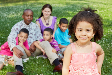 african little girl stands in foreground, her family on grass