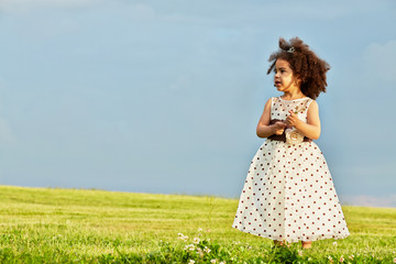 Little girl dressed in polka-dot gown stands alone on meadow