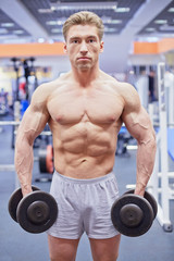 Fototapeta na wymiar Bodybuilder stands with dumbbell in his hands in gym hall