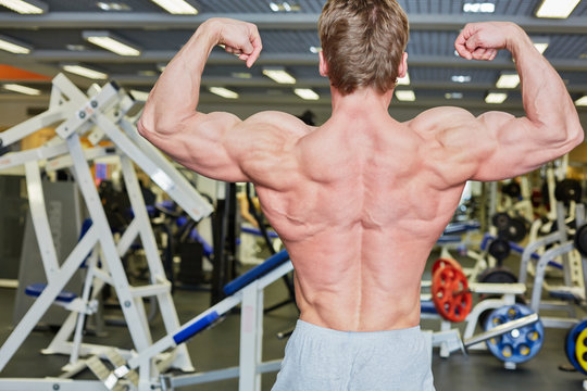 Bodybuilder poses in gym hall demonstrating tense muscles