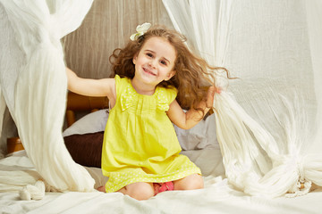 Smiling little girl in yellow dress sits on tent bed © Pavel Losevsky