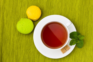 cup of tea and macarons on the green tablecloth