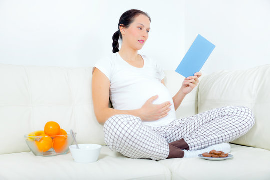 Beautiful pregnant woman reading book  on sofa at home