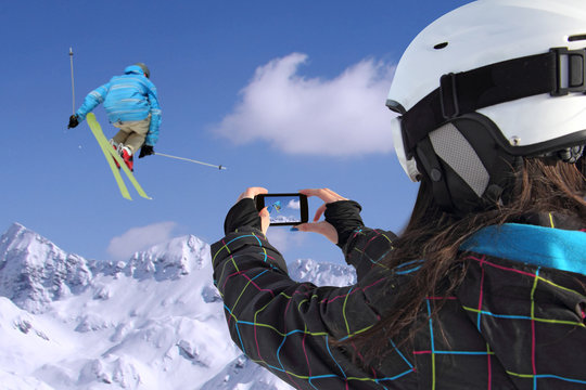 Young girl by mobile phone photographs of skiers jump