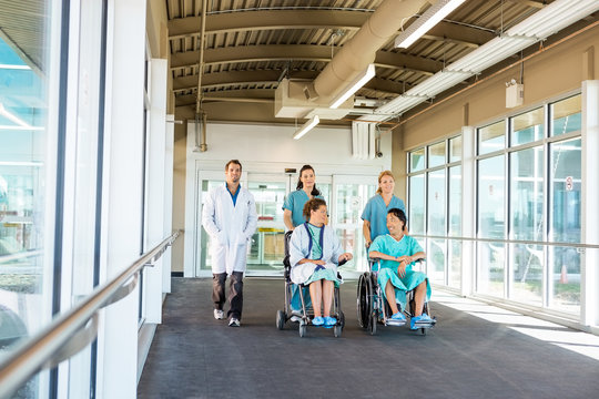 Medical Team With Patients On Wheelchairs At Hospital Corridor