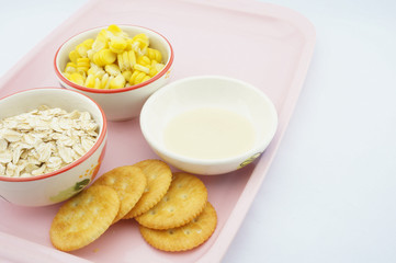 Corn, oats, cracker and sweetened condensed milk on pink tray