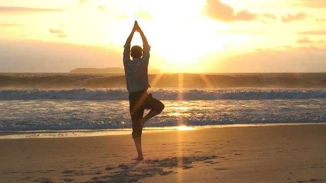Gesch&auml;ftsmann macht Yoga am Strand bei Sonnenaufgang.