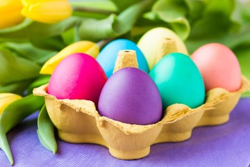 Colorful easter eggs in packing box with tulips flowers