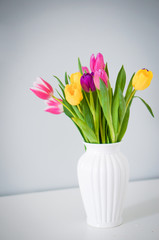 Colorful tulips in white vase on the table on light grey backgro
