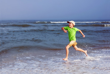 Happy kid sticking his tongue runs along the sea on the surf