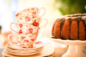 Round cake with chocolate glaze on white stand with tea cups in