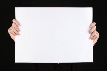 Woman holding blank sign in front her face, isolated on black