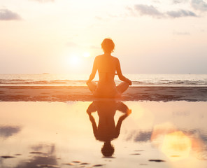 Yoga woman sitting in lotus pose on the beach during sunset.