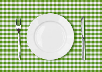 Knife, white plate and fork on green picnic tablecloth