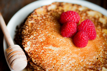 Pancakes with maple syrup and raspberries on wooden background