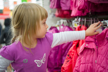 Adorable girl at shopping cart select clothes in supermarket