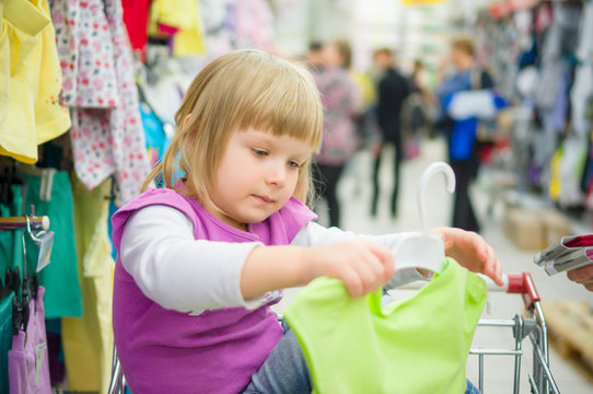 Adorable girl at shopping cart select clothes in supermarket