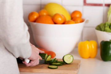 Young caucasian woman is cutting cucumber.
