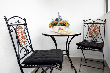 Chairs and a table with artificial flowers and pastry plate.