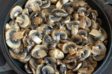 Many sliced fried mushrooms in old black pan closeup