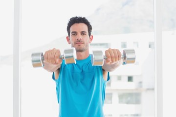 Serious man exercising with dumbbells in fitness studio