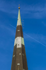Spire against blue sky with jet and contrail