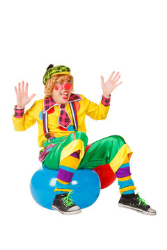Funny clown sits on blue ball isolated on white background