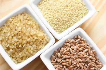Wheat grains, bulgur and couscous on wooden background