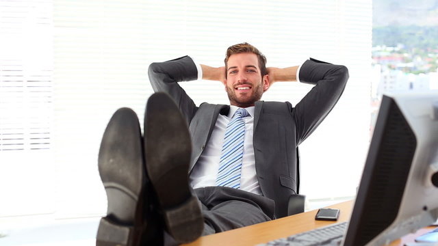 Relaxed businessman putting his feet up smiling at camera