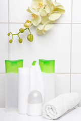 set of white cosmetic bottles with yellow orchid over tiled wall