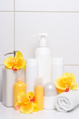 Fototapeta na wymiar set of cosmetic bottles with orange flowers over white tiled wal
