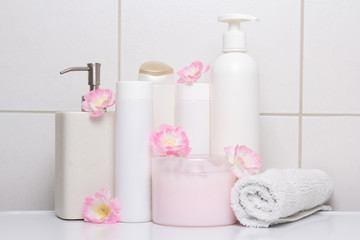 Fototapeta na wymiar set of white cosmetic bottles with pink flowers over tiled wall