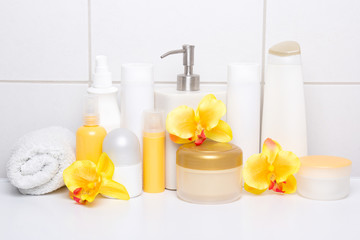 Fototapeta na wymiar collection of white cosmetic bottles with orchids over tiled wal
