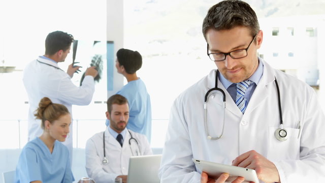 Doctor using tablet while staff are working behind him