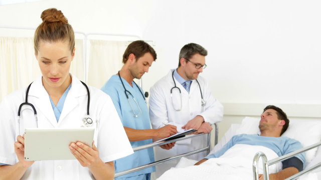 Doctors speaking with sick patient while one checks tablet