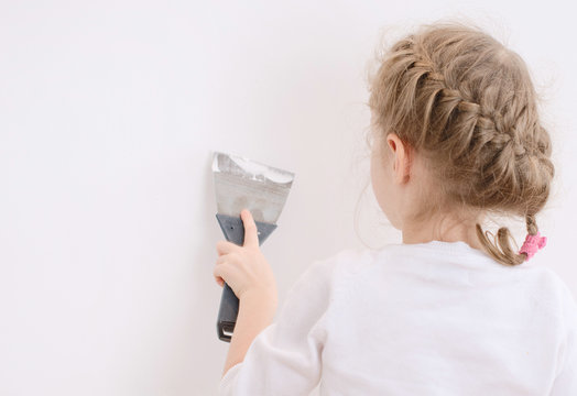 Little girl repairs wall with spackling paste. Place for text.
