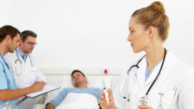 Doctors speaking with sick patient while nurse prepares needle