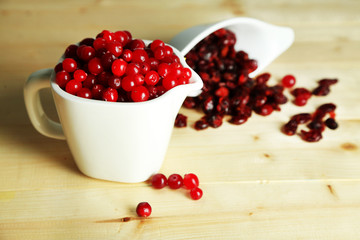 Fresh and dry cranberry in pitchers on wooden table close-up