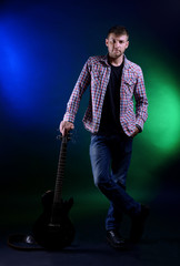 Fototapeta premium Young musician with guitar on dark color background