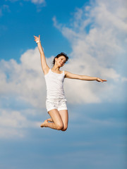 Girl in white hopping with arm raised on background of sky