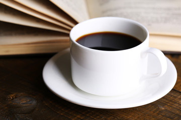Cup of hot coffee with book on wooden background
