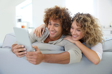 Cheerful couple having fun using tablet in sofa