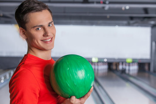 Cheerful young man holding bowling ball.