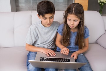 Young siblings using laptop in the living room