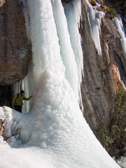 Woman showing a frozen waterfall in the background rock