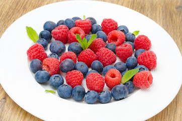 Fresh raspberries and blueberries on a plate on a wooden table
