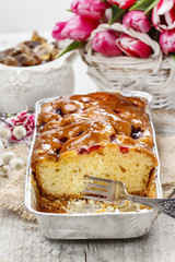 Fruit cake in rectangular pan. Bouquet of pink tulips in the bac
